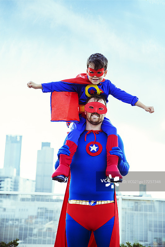 超级英雄父亲在城市屋顶上扛着儿子图片素材