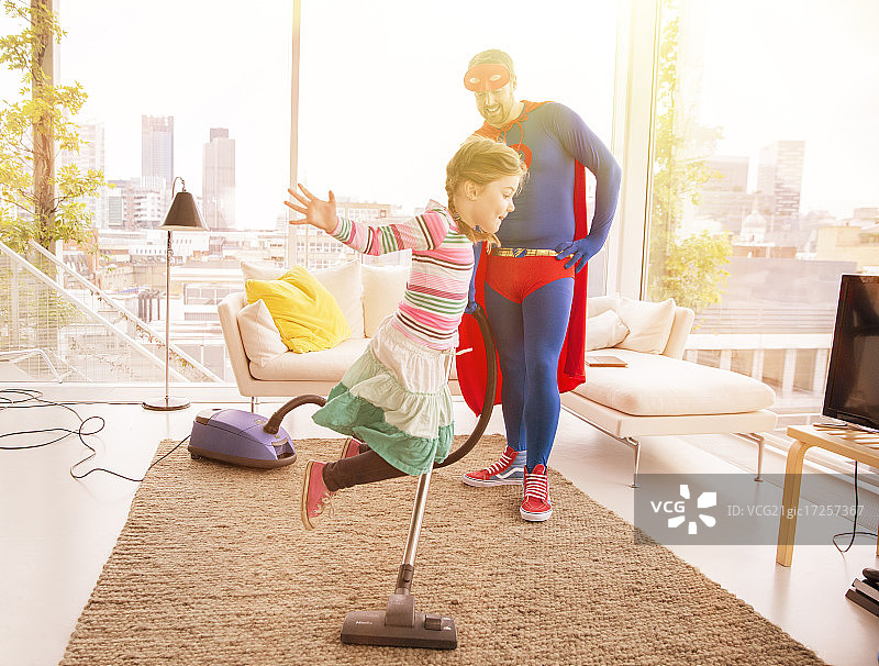 超级英雄父亲在客厅吸尘，女儿跳跃图片素材