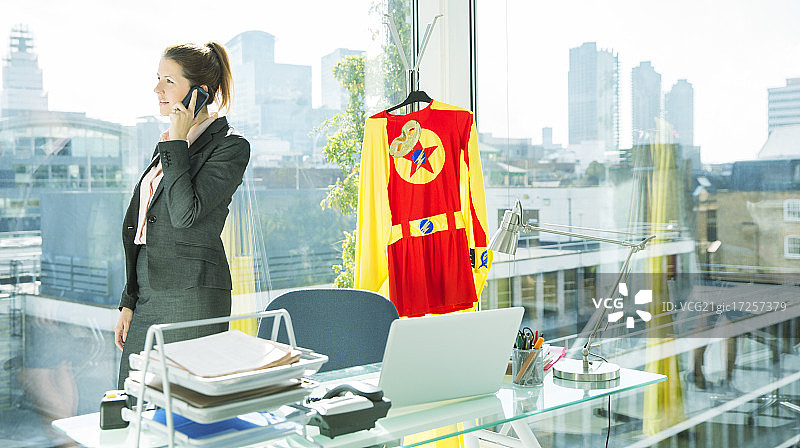 女商人用手机通话，身后是穿着超人服装的人图片素材