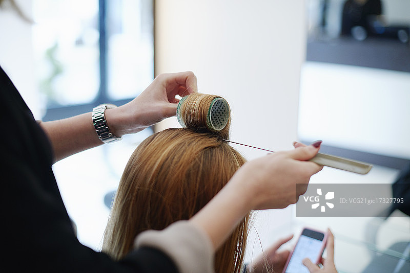 发型师在沙龙里用卷发器卷顾客的头发图片素材