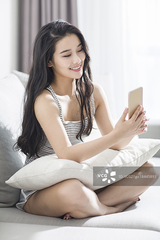 年轻女子坐在沙发上玩手机图片素材