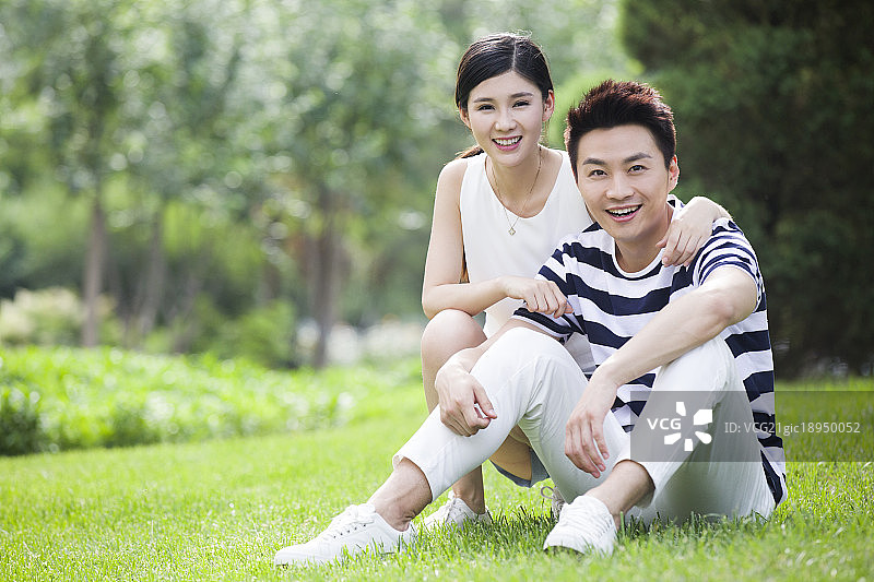 快乐的年轻情侣坐在草地上图片素材