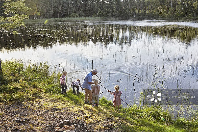 爷爷在阳光明媚的湖边教孙辈钓鱼图片素材