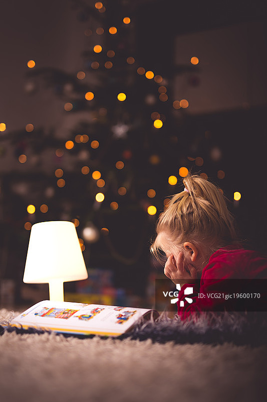 女孩在圣诞树旁边的灯光下看书图片素材