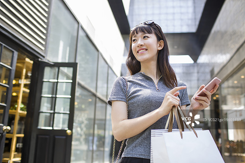 快乐的年轻女子拿着手机和购物袋图片素材