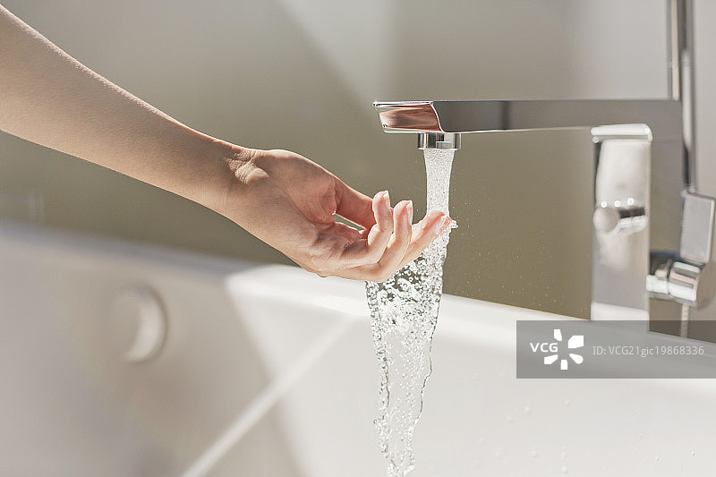 女子触摸现代浴缸水龙头流出的水图片素材
