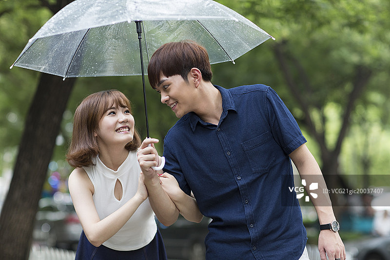 快乐的年轻情侣打着雨伞散步图片素材