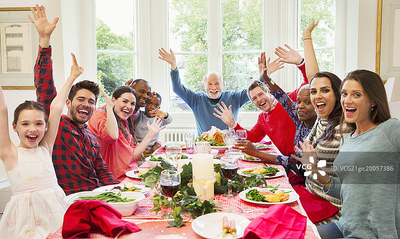 在圣诞晚餐桌上挥手致意的热情多元民族家庭肖像图片素材