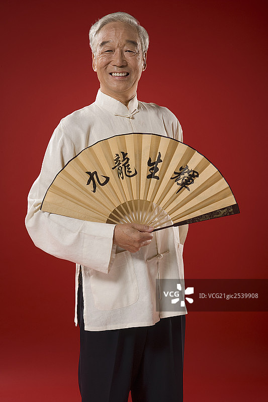 一位老人手拿一把写有“九龙生辉”的扇子图片素材