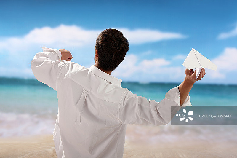 东方男人在海滩扔纸飞机图片素材