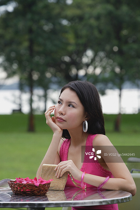 年轻女人坐在户外桌旁，手托着下巴，看向别处图片素材