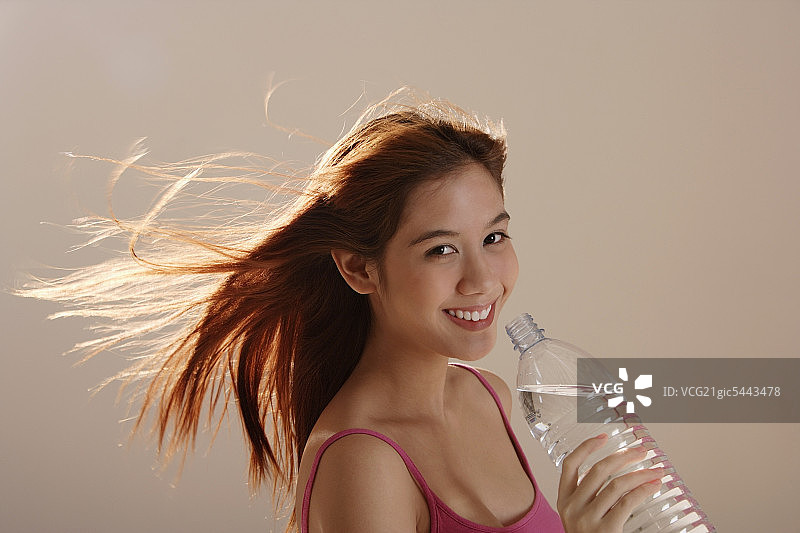 手持瓶装水、头发飘逸的亚洲女孩图片素材