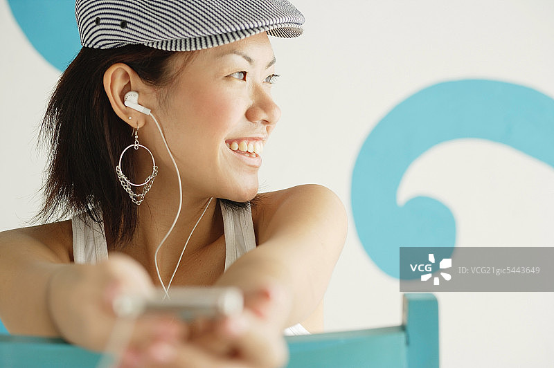 戴着贝雷帽，听着MP3播放器，看向别处，微笑的年轻女人图片素材