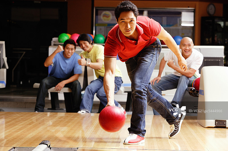 男人在打保龄球，朋友们在背景中欢呼图片素材