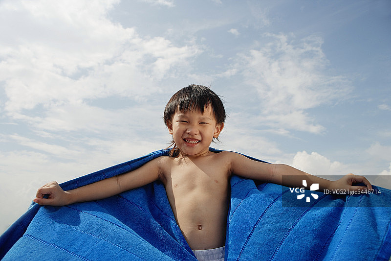 在海滩上玩耍的男孩，蓝色毛巾在身后飞舞图片素材