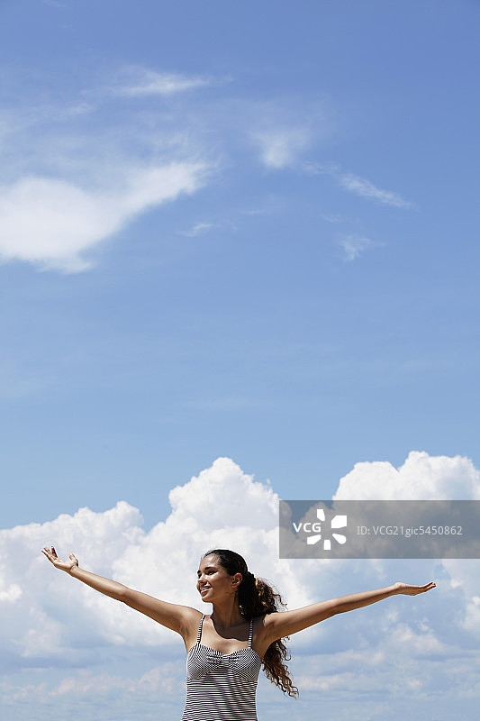 快乐的年轻女人在蓝天白云下举起双臂图片素材