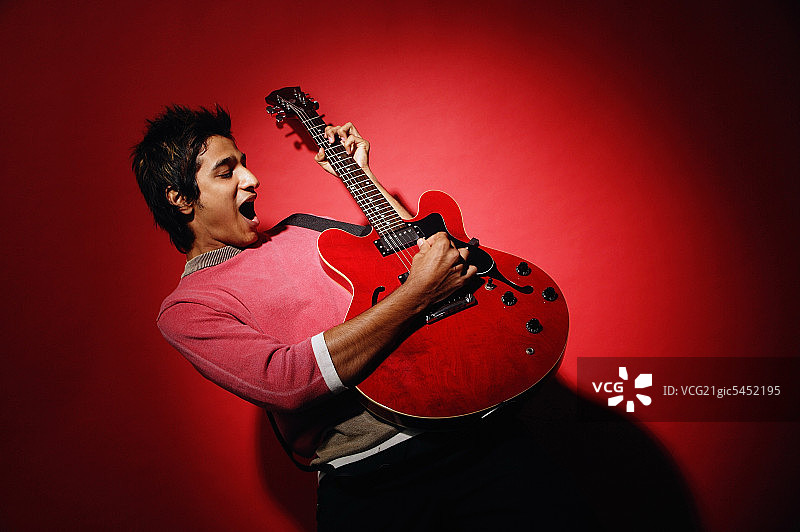 青年男子靠在红墙边弹吉他图片素材