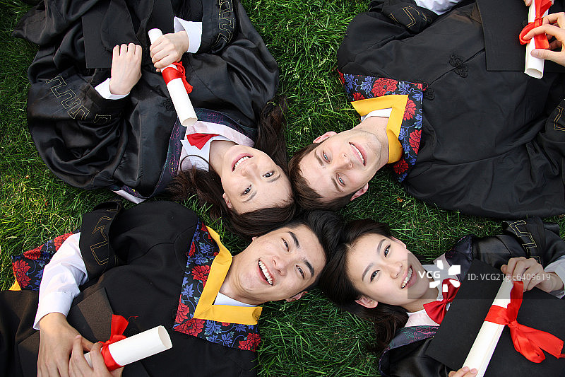 四个身穿学士服的大学生躺在草地上图片素材
