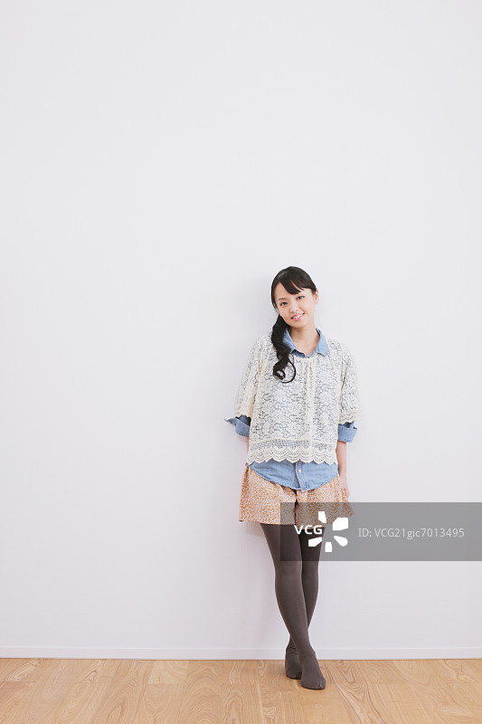 年轻女子靠在白墙上对着镜头微笑图片素材