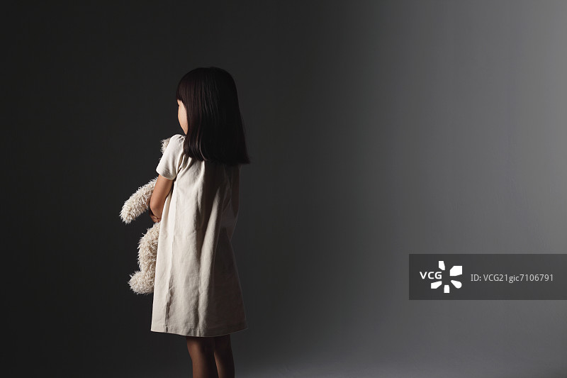 穿着白色连衣裙，在墙前抱着泰迪熊的女孩图片素材