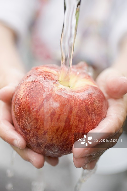 孩子的手在流水下拿着红苹果图片素材