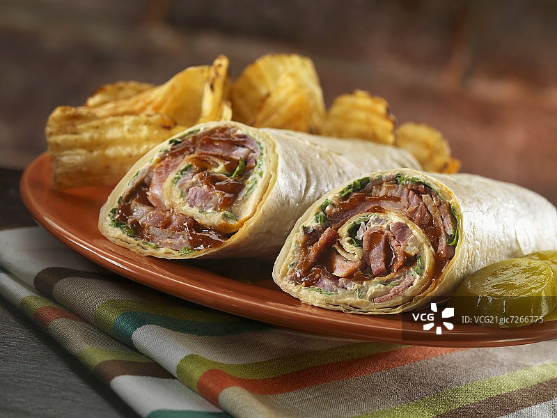 夹有美式奶酪、奇波雷蛋黄酱和生菜的牛胸肉卷；薯条和泡菜图片素材