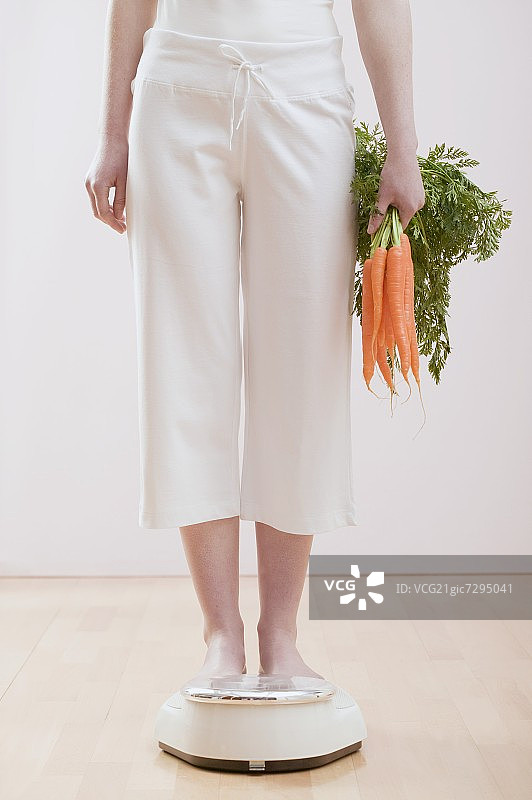在浴室秤上放着胡萝卜的年轻女子图片素材