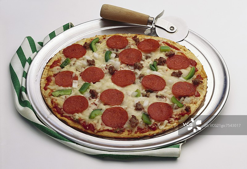 披萨盘上的意大利辣香肠、香肠、辣椒和洋葱披萨与切割器图片素材