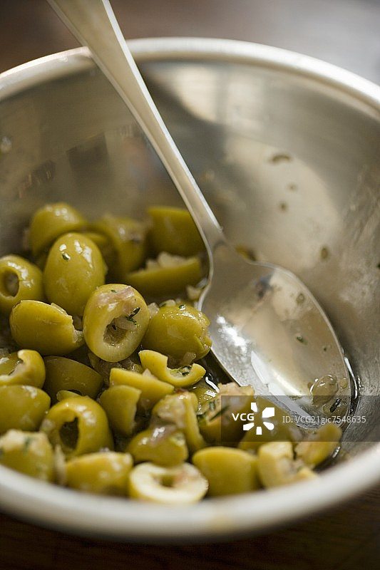 金属碗中盛放的绿色橄榄和勺子图片素材