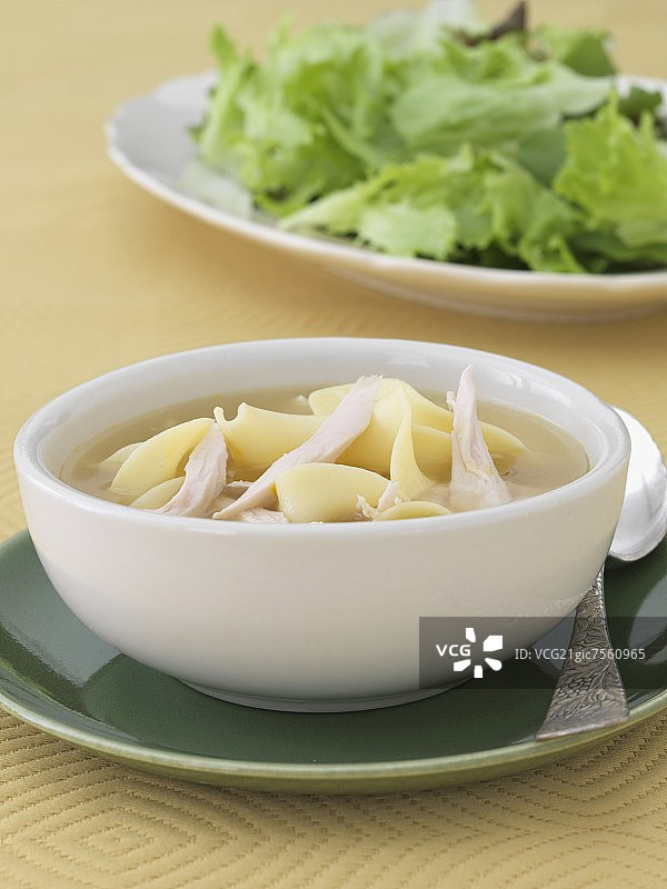 鸡肉面条汤碗；背景是配菜沙拉图片素材