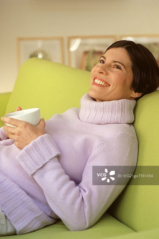 年轻女人在沙发上喝茶或咖啡图片素材