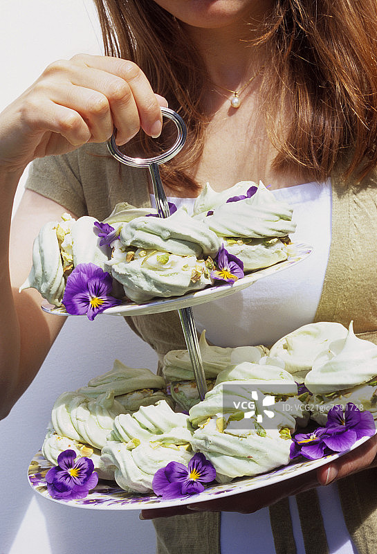 年轻女子托着装有开心果蛋白酥皮的多层架图片素材