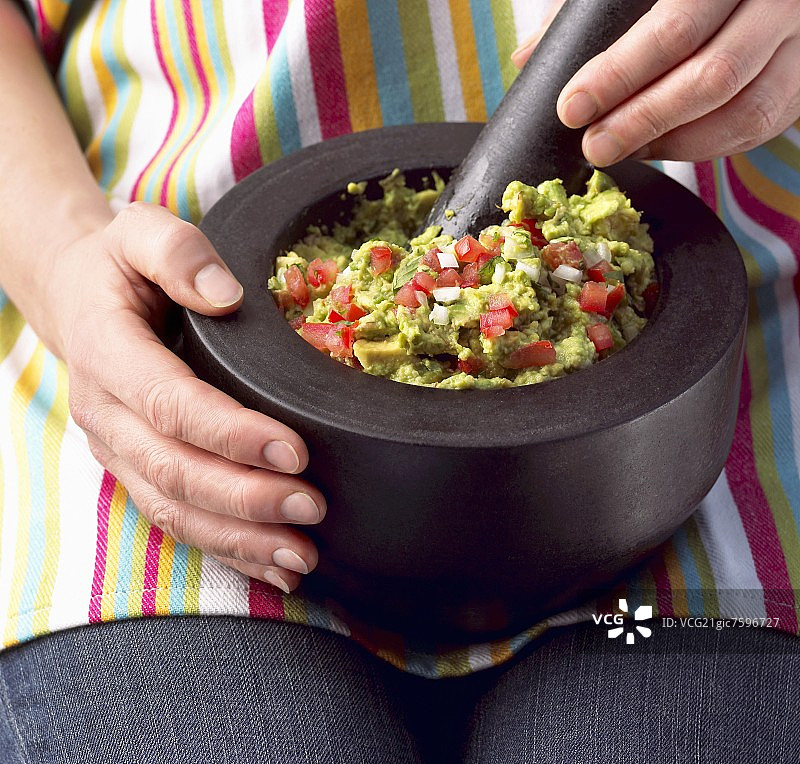 用研钵和杵在膝盖上制作鳄梨酱的女人图片素材