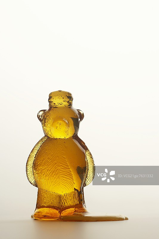 从打开的蜂蜜熊中溢出的蜂蜜，白色背景图片素材