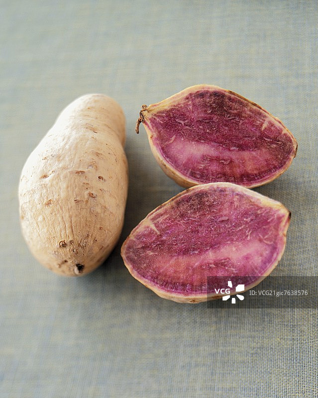 编织绿色面料上的完整和切半的紫薯图片素材