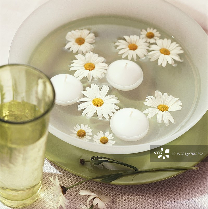碗中的玛格丽特雏菊与漂浮的蜡烛图片素材