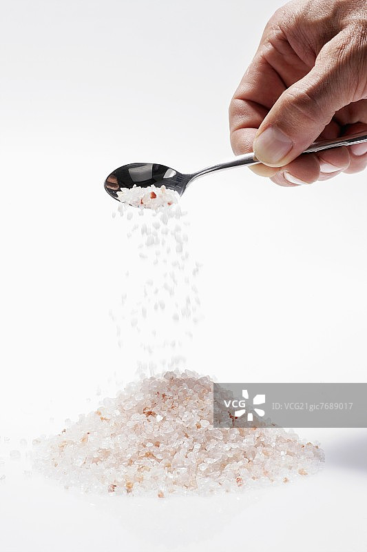 用勺子将喜马拉雅盐撒到盐堆上图片素材