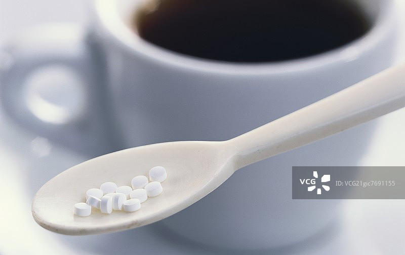 咖啡杯前的勺子上的甜味剂片图片素材