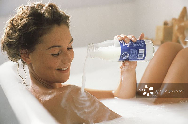 在牛奶浴中，将牛奶倒在肩上的年轻女人图片素材