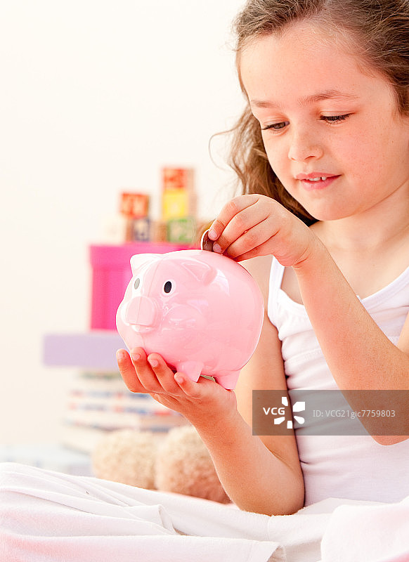 可爱小女孩在家中床上往储蓄罐里存钱图片素材