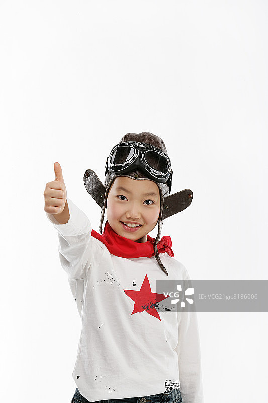 戴着飞行帽、飞行护目镜和围巾的女孩（12-13岁）竖起大拇指，面带微笑，肖像图片素材