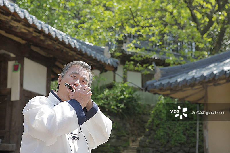 身穿韩国传统服装的老年男人正在吹口琴图片素材