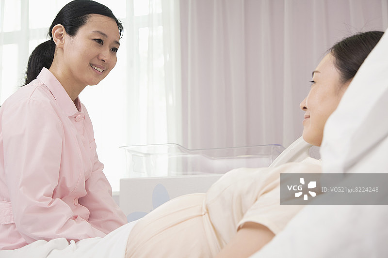 微笑的护士与躺在医院病床上的孕妇交谈图片素材