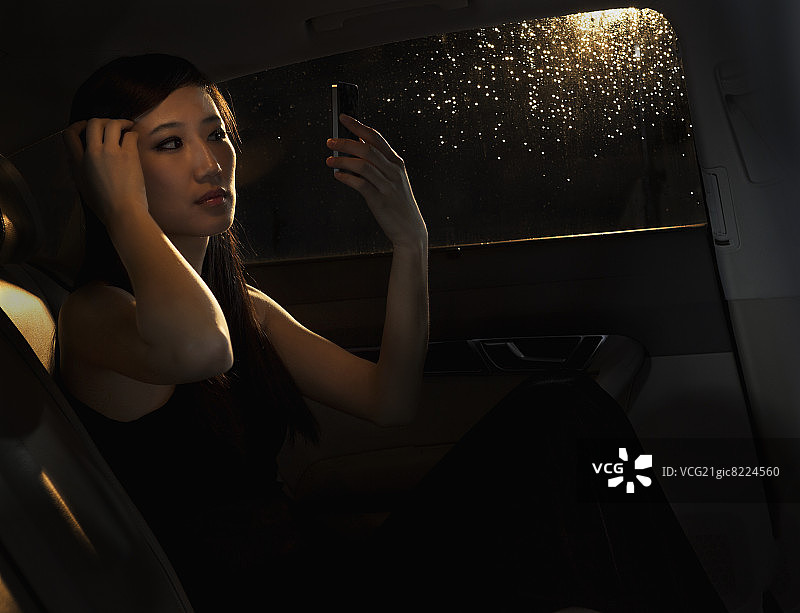 年轻女人坐在北京雨夜的车里，在出门前用手机整理头发图片素材