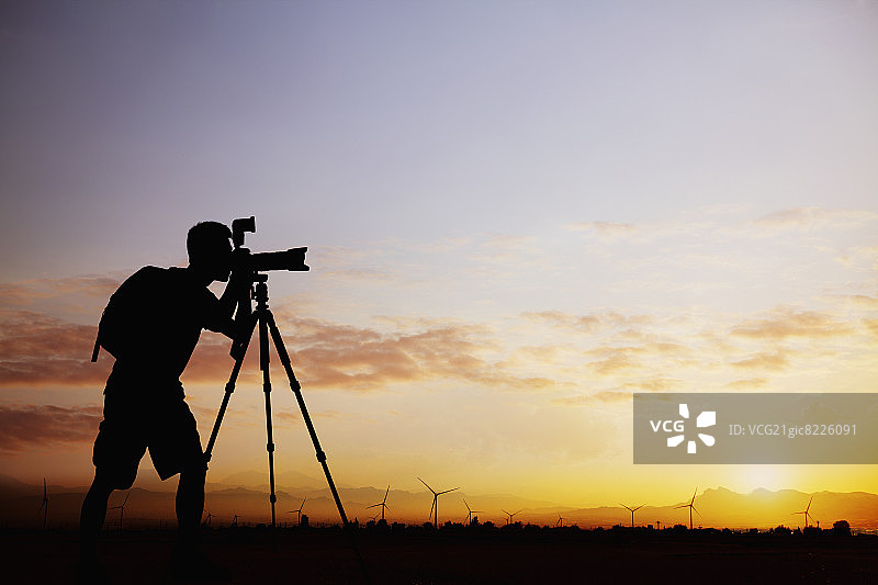 在戏剧性天空的日落时用相机拍照的男子轮廓图片素材