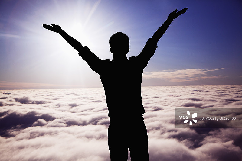 举起双臂的年轻男子轮廓，背景是天空图片素材
