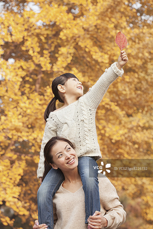 女儿骑在母亲的肩上欣赏秋叶图片素材