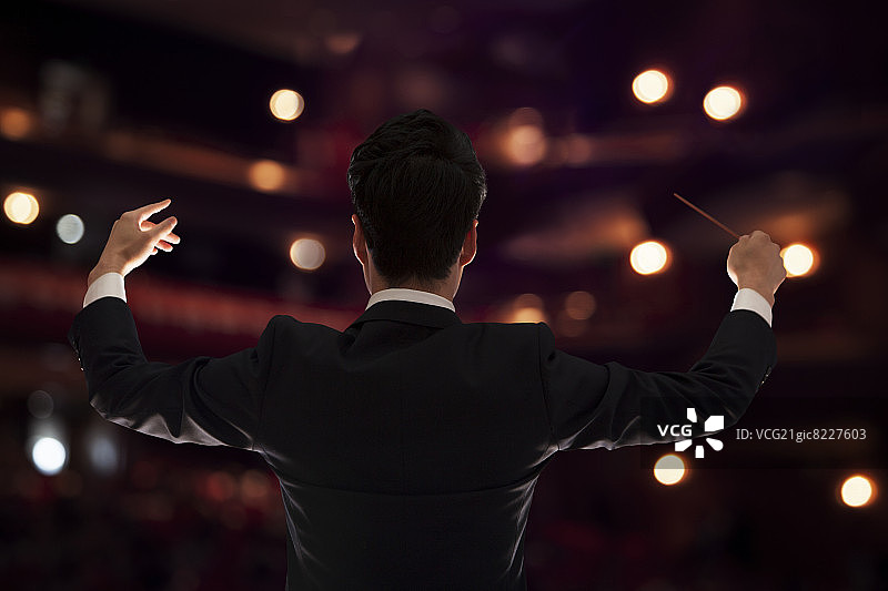 年轻指挥家在演出中举起指挥棒（背面视角）图片素材