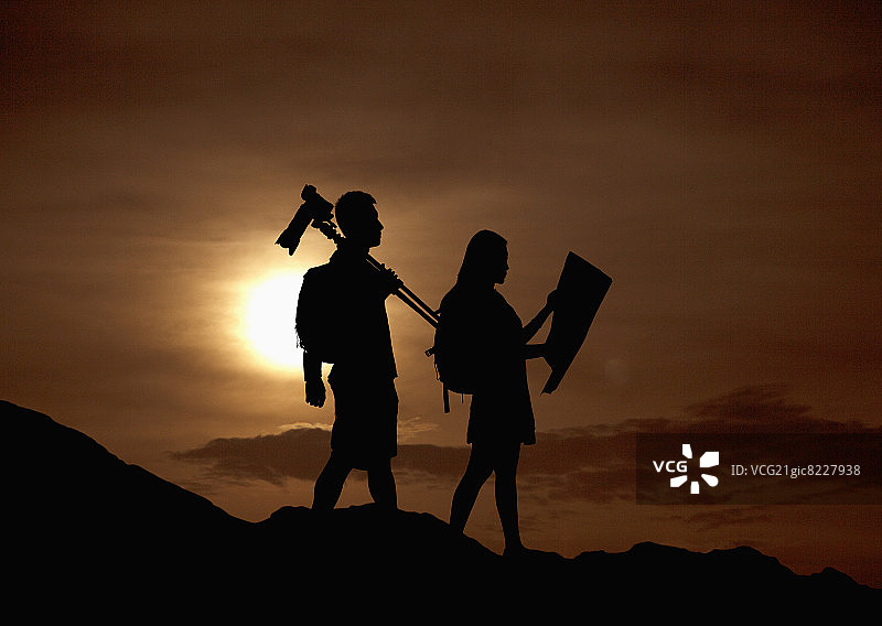 日落时分，在自然界中徒步旅行并携带相机和地图的两个人的轮廓图片素材