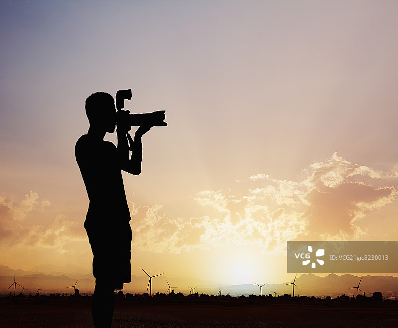 在戏剧性天空的日落时用相机拍照的男子轮廓图片素材